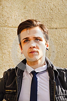 Close up portrait of stylish attractive young man standing against wall outside on sunny day