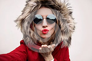 Close up portrait of stylish cool woman blowing red lips sending sweet air kiss stretching hand for taking selfie