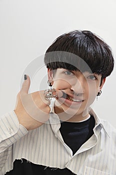 Close-up portrait of stylish young man with piercing making faces, posing  over grey studio background