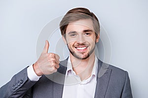 Close up portrait of successful handsome young man in formal wear showing gesture like with beaming smile while standing on gray