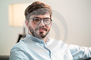 A close-up portrait of a successful young man with a beard and glasses