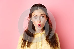 Close up portrait of surprised brunette girl saying wow, folding lips and stare amazed at camera, checking out awesome