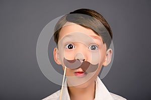 Close up portrait of surprised funny schoolboy holding paper mustache