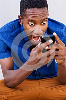 Surprised african man looking at his mobile phone and screaming