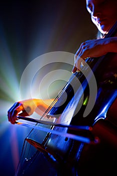 Close up portrait of talented young woman, musician, cellist performing symphony in purple-blue spotlights on stage with