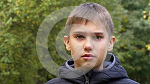 Close up portrait of teenage boy in black jacket outdoors with city park trees in background. 4K video