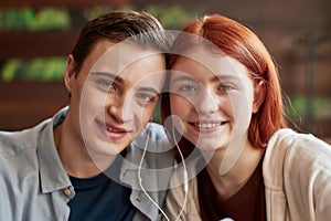 Close up portrait of teenage couple smiling at camera while listening to music together using same pair of earphones