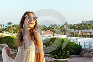 Close up portrait of a teenage girl in white dress and Sunglasses in a park during a sunny day, looking and smiling against the sk