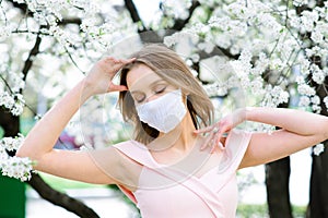Close up portrait of tender girl under a blossoming cherry tree with a mask from the coronavirus