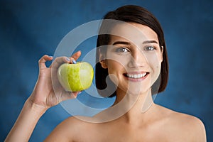 Close up portrait of tender young girl holding apple over blue background