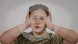 Close-up portrait of terrified military woman looking at camera closing ears with hands. Scared young beautiful
