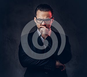 Close-up portrait of a thoughtful stylish businessman with serious face in an elegant formal suit and glasses on a dark