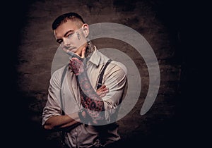 Close-up portrait of a young old-fashioned tattooed guy wearing white shirt and suspenders. on dark background.