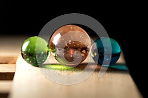 A close up portrait of three different colored marbles on a wooden surface casting colorful reflections. The glass spheres are