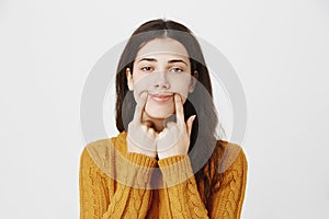 Close-up portrait of tired and gloomy caucasian pierced girl stretching mouth with fingers, making fake smile while