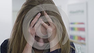 Close up portrait of tired lady in formal clothes with tousled hair having headache in the office. Woman grabbing her