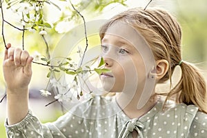 Close-up portrait of a toddler girl with red hair in front of a cherry blossom. Spring