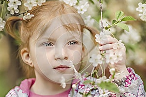 Close-up portrait of a toddler girl with red hair in front of a cherry blossom. Spring