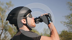 Close up portrait of triathlete in black helmet and glasses drinking water. Bearded male cyclist drinks water from water bottle. S