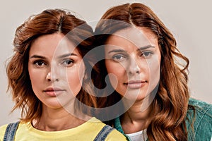 Close up portrait of two attractive young girls, twin sisters looking at camera, posing together isolated over light