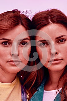 Close up portrait of two attractive young girls, twin sisters looking at camera, posing together isolated over pink