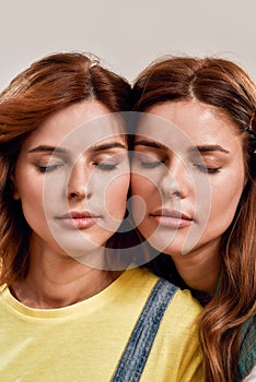 Close up portrait of two attractive young girls, twin sisters posing together with eyes closed isolated over light
