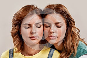 Close up portrait of two attractive young girls, twin sisters posing together with eyes closed isolated over light