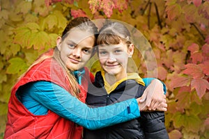 Close-up portrait of two girls of Slavic appearance in casual autumn clothes against the background of an autumn forest