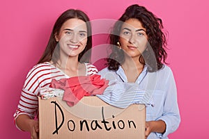 Close up portrait of two girls volunteering, women holding paper box with clothes for poor people, friends making donation,