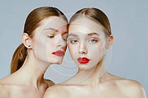 Close-up portrait of two gorgeous young fashion models with red lips posing grey background.