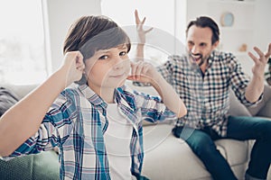 Close-up portrait of two guys dad and pre-teen son sitting on couch covering closing ears having fight disagreement in