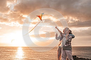 Close up and portrait of two old and mature people playing and enjoying with a flaying kite at the beach with the sea at the