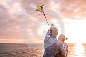 Close up and portrait of two old and mature people playing and enjoying with a flaying kite at the beach with the sea at the