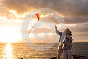 Close up and portrait of two old and mature people playing and enjoying with a flaying kite at the beach with the sea at the