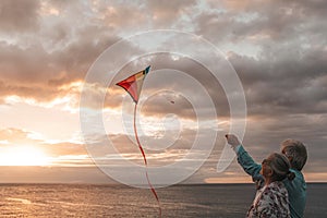 Close up and portrait of two old and mature people playing and enjoying with a flaying kite at the beach with the sea at the