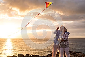 close up and portrait of two old and mature people playing and enjoying with a flaying kite at the beach with the sea at the