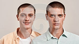 Close up portrait of two young caucasian twin brothers posing together in studio, looking at camera with different face