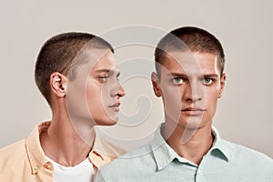 Close up portrait of two young caucasian twin brothers posing together in studio, standing isolated over beige