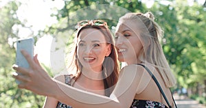 Close up portrait of two young cheerful girls having fun and making selfie, outdoors.