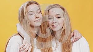 Close up portrait of two young redhead twin sister hugging and showing peace gesture to camera, orange studio background