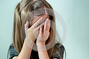 Close-up portrait of unhappy little girl with long hair covering her face with hands crying