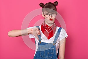 Close up portrait of unimpressed disliking attractive female student dresses denim overall, white t shirt and red bandana, showing