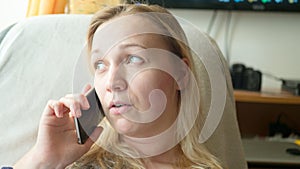 Close-up portrait of upset, sad, depressed and worried blonde woman talking on the phone in the apartment