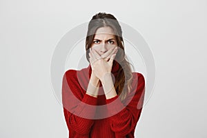 Close up portrait of upset scared european woman, covering mouth with both hands to prevent screaming sound, after