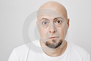 Close-up portrait of upset tired unhappy bearded bald man, looking tired, standing against gray background. Exhausted