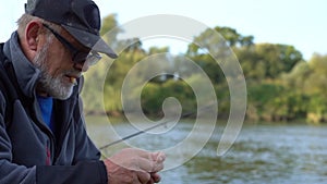 Close up portrait view of an old fisherman in a cap and glasses and with a cigarette in his mouth angling with a rod in