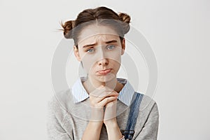 Close up portrait woman with brown hair in double buns pouting with pity look holding hands like praying. Pathetic photo
