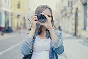 Close up portrait of woman in casual clothes taking photo on her digital camera. Lens is in focus, blurred city street is on the b