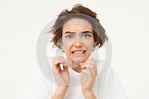 Close up portrait of woman cringing, looking disgusted, jumps from fear and looks afraid, stands over white background