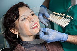 Close-up portrait of woman in dental clinic office. Dentist checking and selecting colour of the teeth. Dentistry